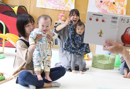 母親が子どもを抱いたり、子どもの腕を伸ばしたりして、動きながら一緒に絵本を楽しむ親子の様子